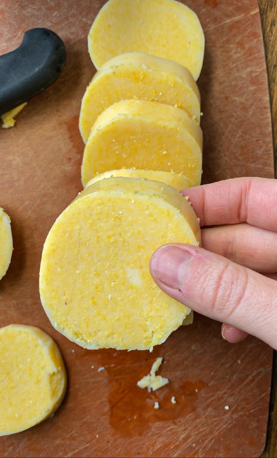 A hand holding an uncooked polenta round that has just been cut