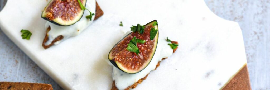 A close up shot of a fresh fig on a cracker with blue cheese on the cracker and parsley on the fig