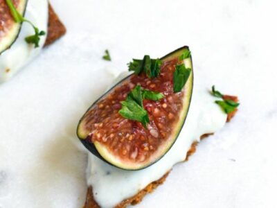 A close up shot of a fresh fig on a cracker with blue cheese on the cracker and parsley on the fig