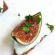 A close up shot of a fresh fig on a cracker with blue cheese on the cracker and parsley on the fig
