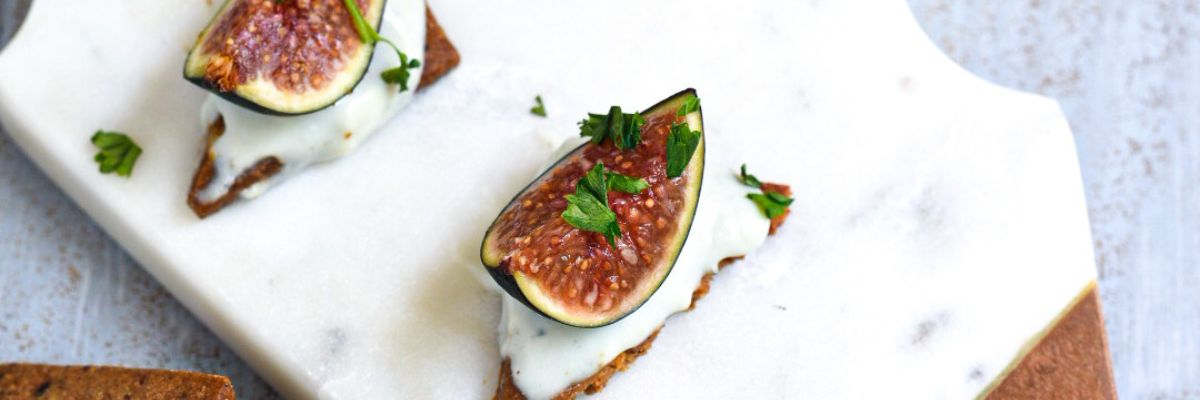 A close up shot of a fresh fig on a cracker with blue cheese on the cracker and parsley on the fig
