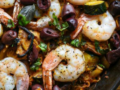close up shot of a cast iron skilled with cooked orzo, shrimp, shiitake mushrooms and baked olives recipe