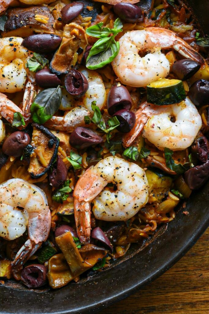close up shot of a cast iron skilled with cooked orzo, shrimp, shiitake mushrooms and baked olives recipe