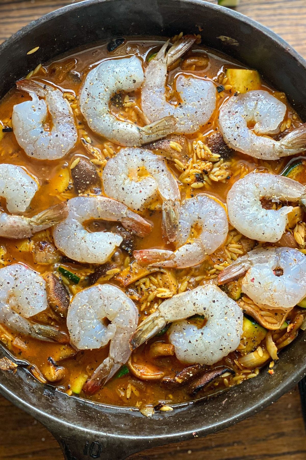 a large skillet with cooking liquid, orzo and raw shrimp over the top
