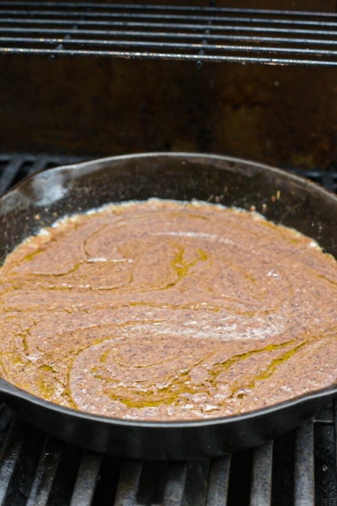 A large cast iron skillet on a grill filled with a black bean sauce recipe with oil swirls in the sauce