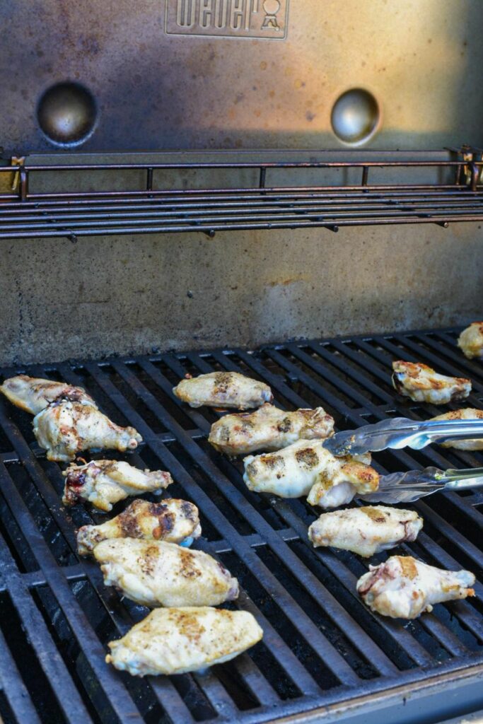 two rows of chicken wings on a grill with tongs flipping one wing