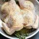 A spatchcocked whole chicken in a stainless steel skillet with rosemary under it