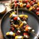 A black plate with 4 kabobs on top filled with bright grilled vegetables and lemon dill chicken, with a greek yogurt sauce drizzled over the top
