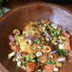 A close up image of mediterranean baked cod recipe, with a golden baked white fish filet topped with green olives, red onion, parsley and tomatoes
