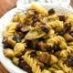 A large white porcelain serving bowl filled with fusilli pasta and roasted eggplant, olives and artichoke hearts