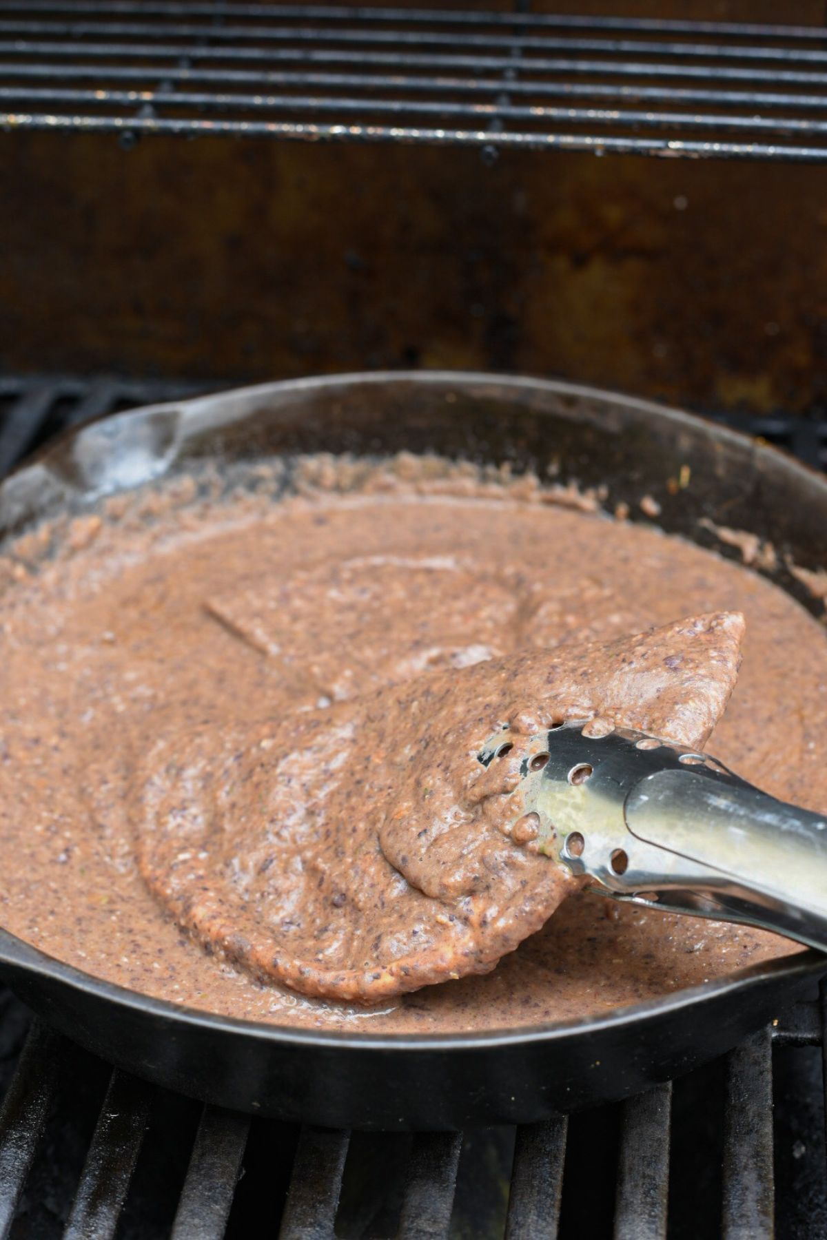 A grilled pita pocket being lifted out of an enfrijoladas sauce with tongs