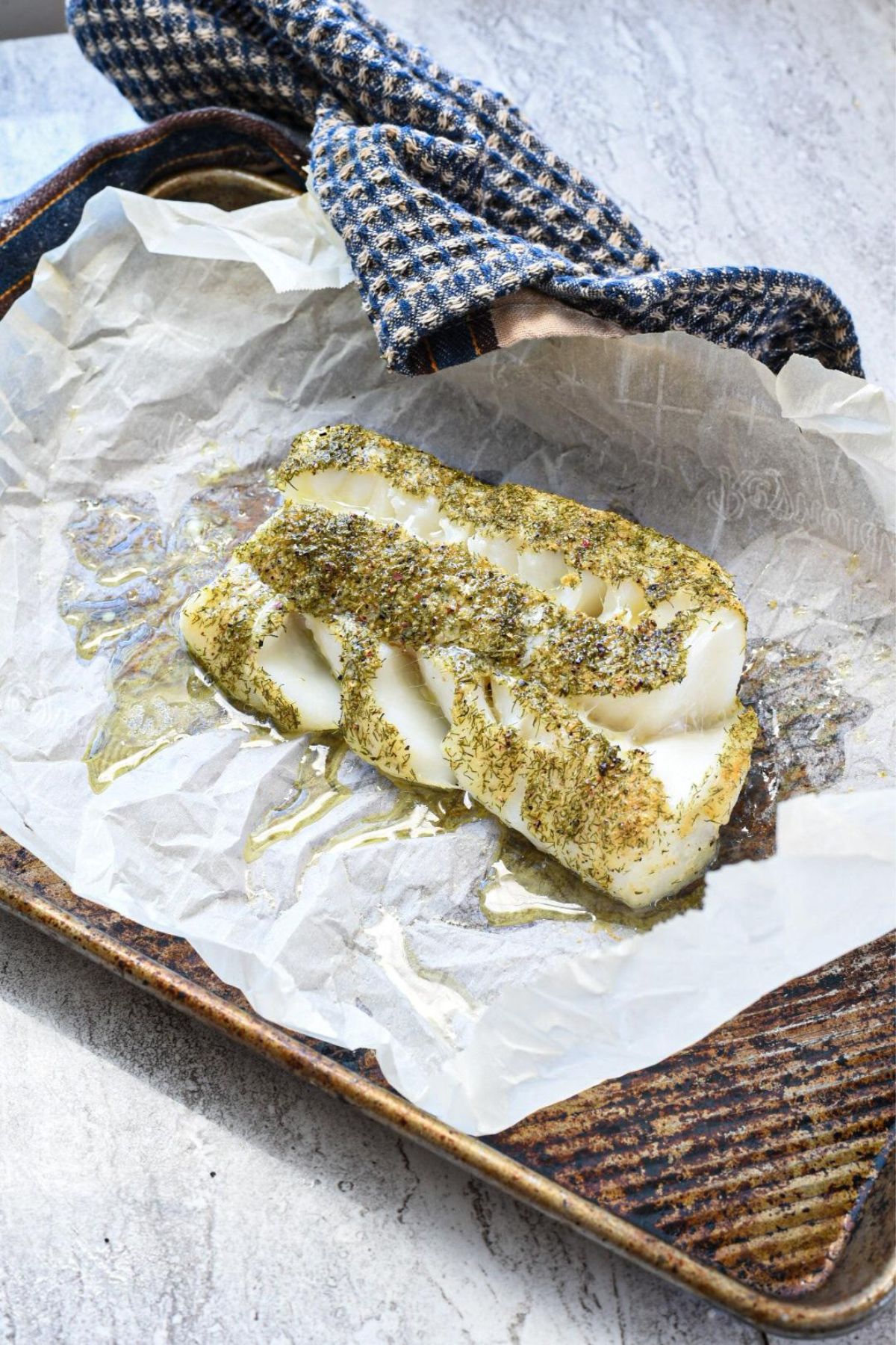 A piece of cooked cod fish sprinkled with dill herb on a parchment paper lined baking sheet