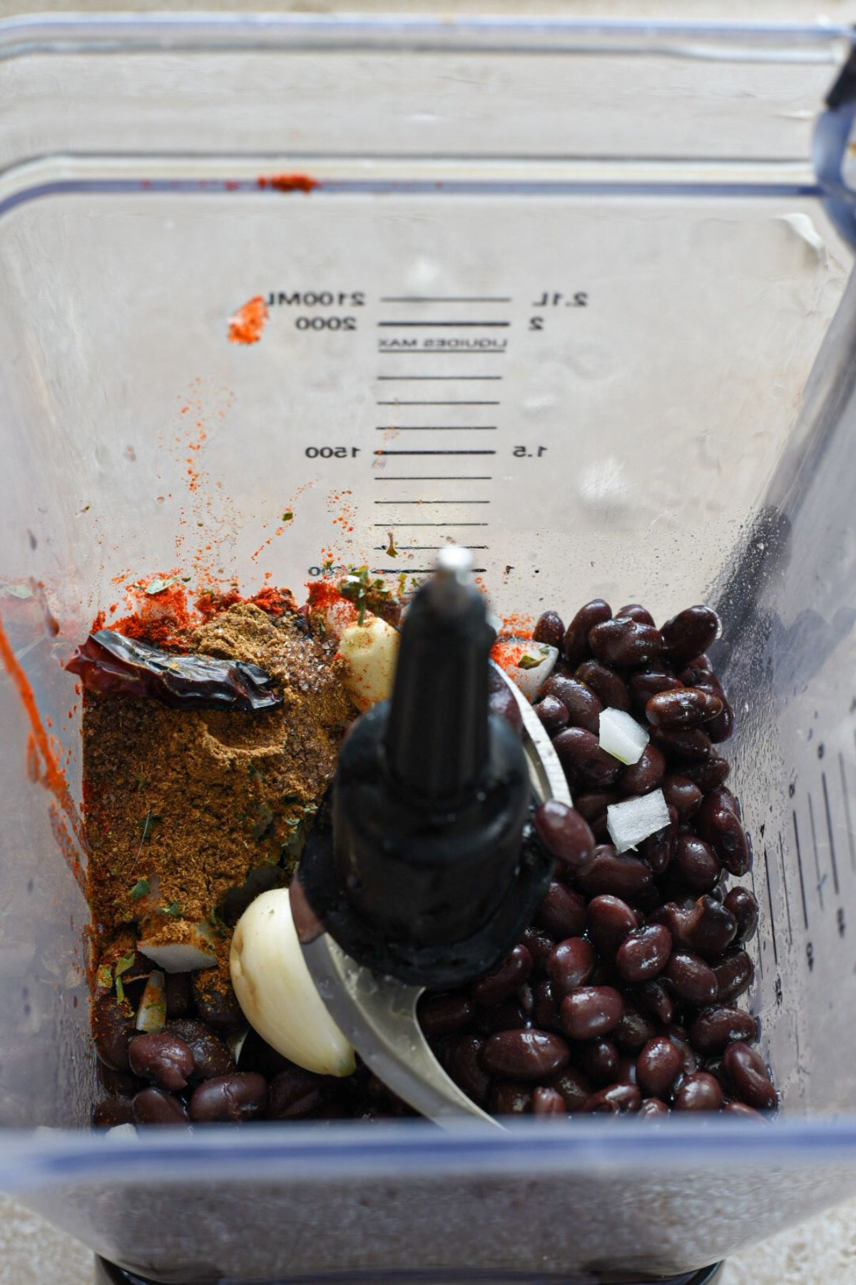An overhead shot of the ingredients used to make enfrijoladas sauce, including black beans, onion, garlic, spices, chili pepper