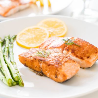 A white plate filled with two pieces of cooked salmon, lemon slices and asperagus