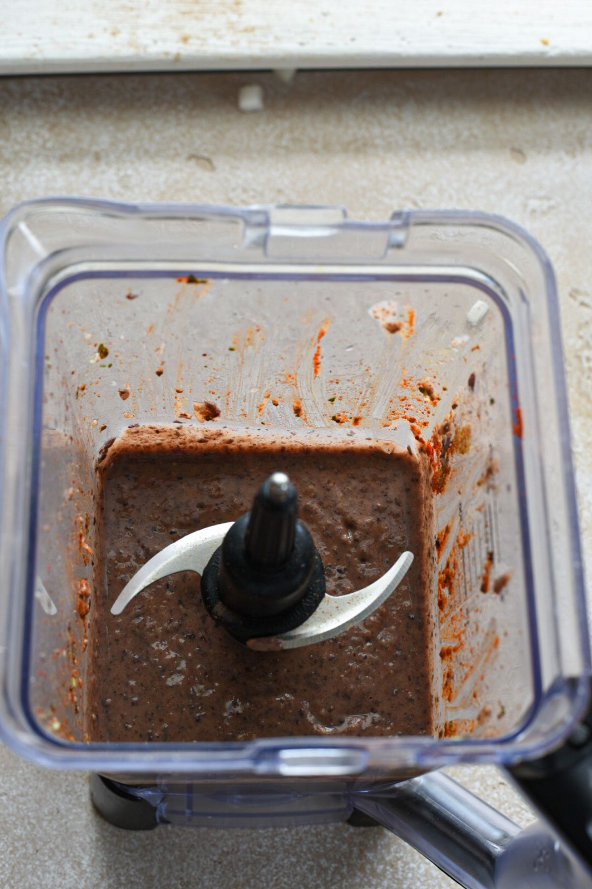 An overhead shot of the inside of a blender, filled with a blended brown enfrijoladas bean sauce