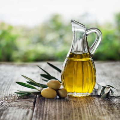 A glass pitcher filled with olive oil on a wooden surface with olives next to it