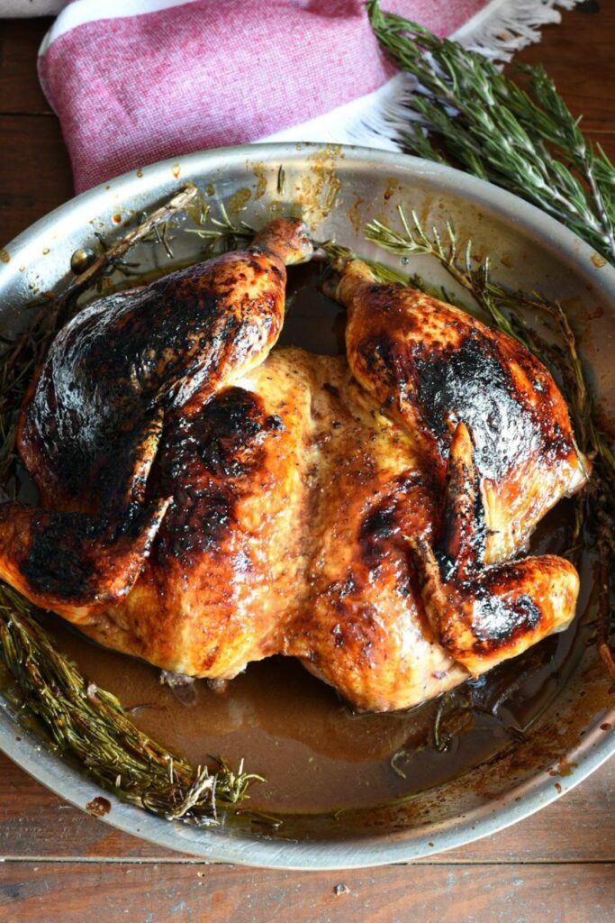 An overhead shot of a cooked spatchcocked chicken in a stainless steel skillet with rosemary underneath it