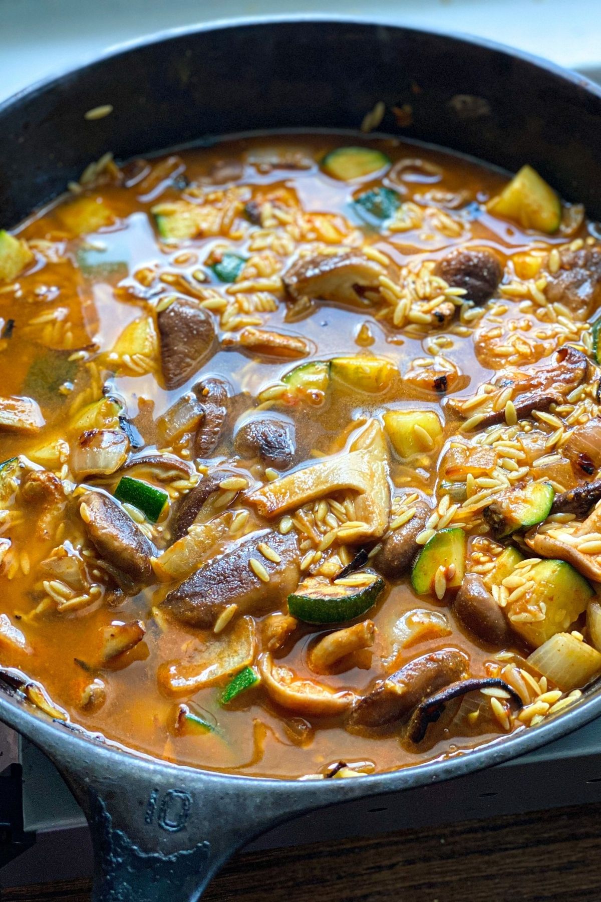 a skillet filled with sauteed vegetables, orzo pasta and a golden broth