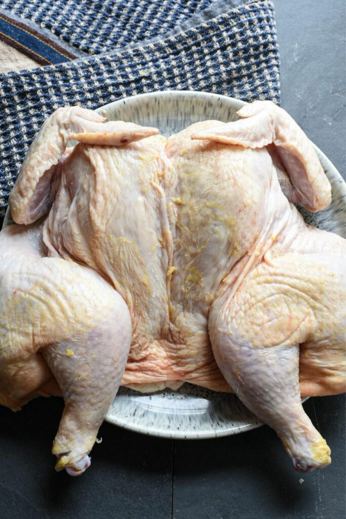 An overhead shot of a spatchcock chicken on a plate with a towel underneath the plate