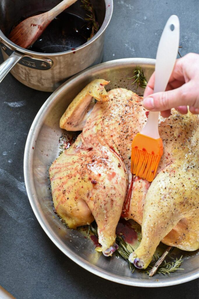 Spatchcock chicken in a skillet being brushed with pomegranate sauce