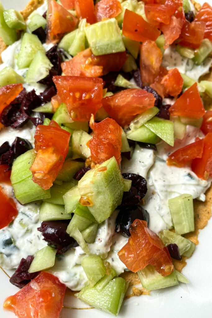 A close up shot of a 7 layered dip with hummus, tzatziki, tomatoes, cucumber, olives and feta