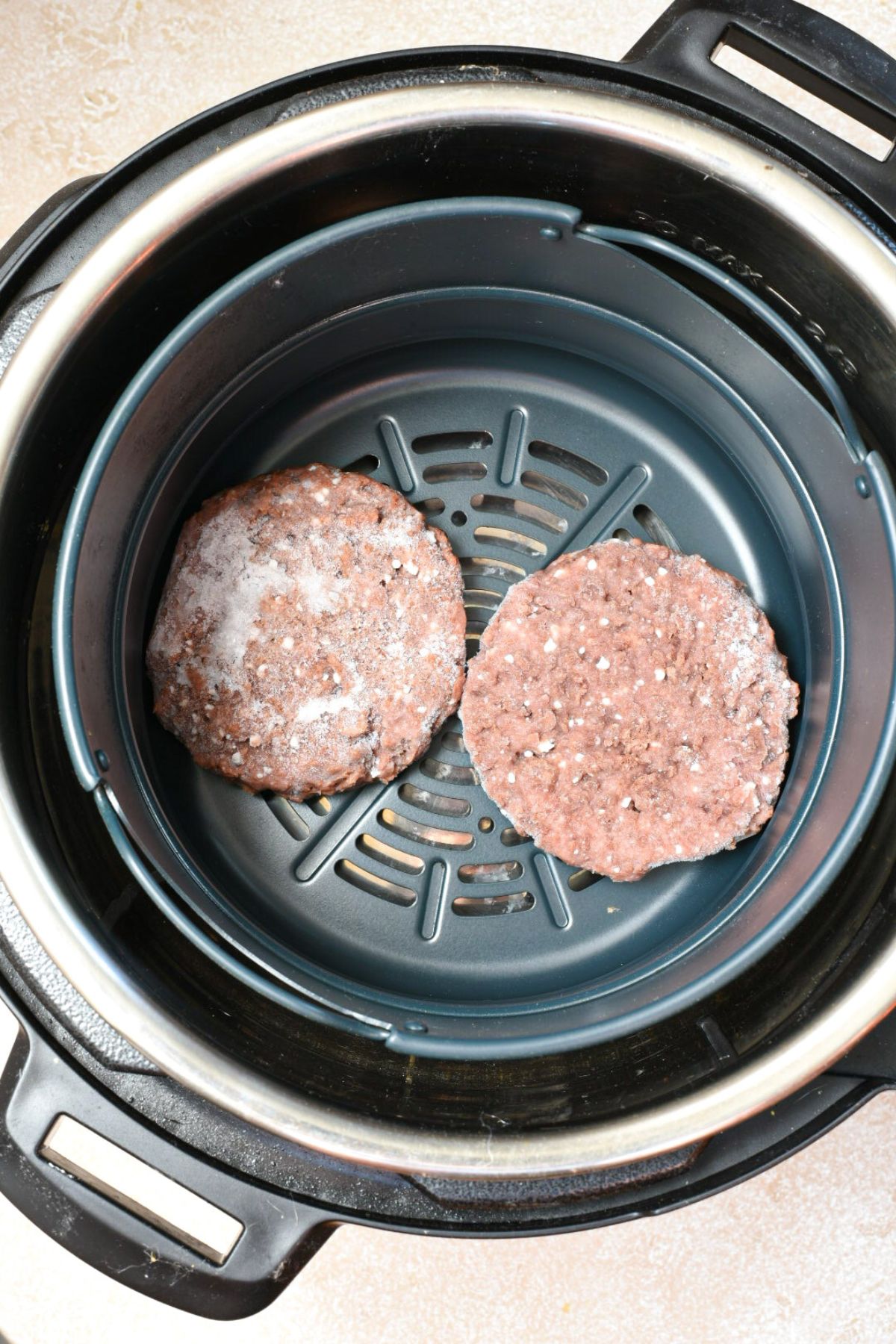An overhead shot of the inside of an air fryer with two frozen beyond burger patties inside of the air fryer basket