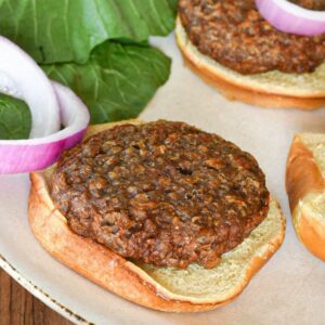 A beyond beef burger on a burger bun with red onion slices and greens behind them, and mustard in the corner of the shot