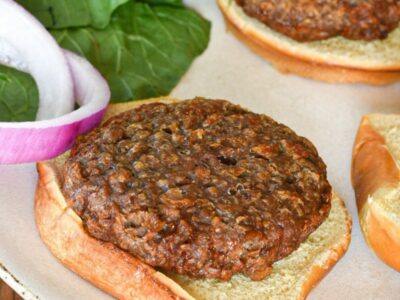 A beyond beef burger on a burger bun with red onion slices and greens behind them, and mustard in the corner of the shot