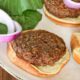 A beyond beef burger on a burger bun with red onion slices and greens behind them, and mustard in the corner of the shot