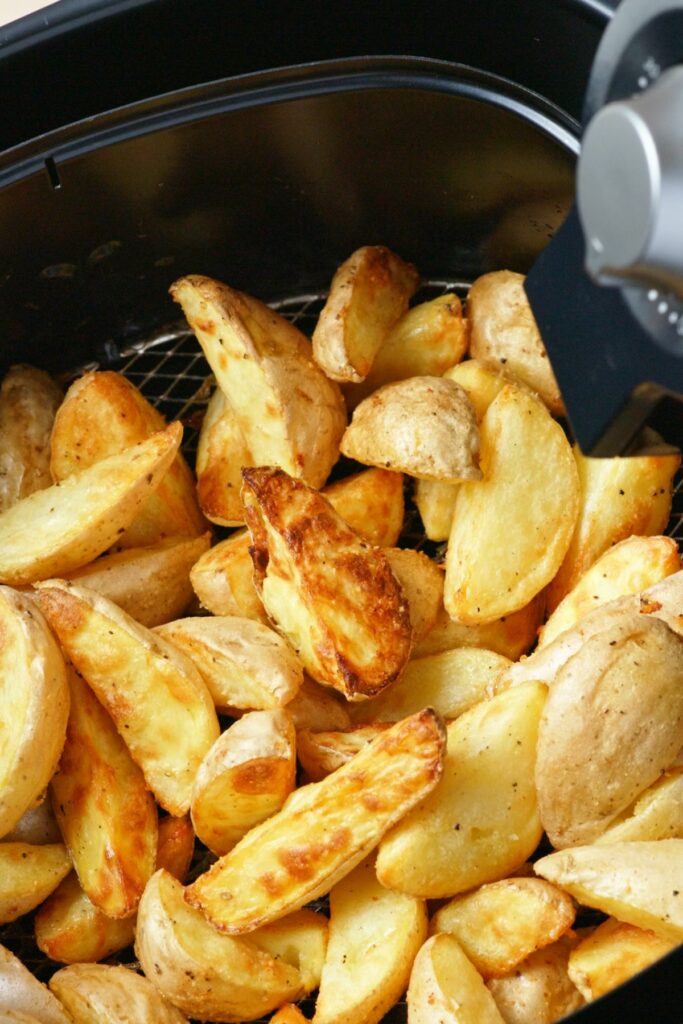 a bunch of crispy brown and golden wedge cut french fries inside of an air fryer