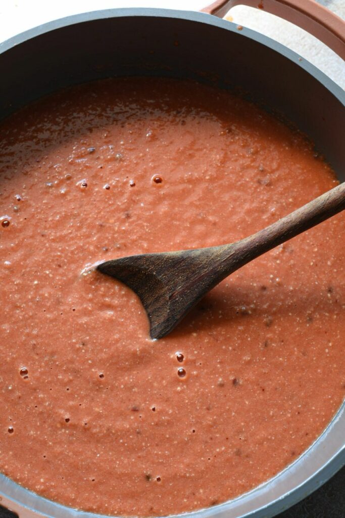 An overhead shot of a pan filled with red arrabiata sauce, with a wooden spoon in the middle.