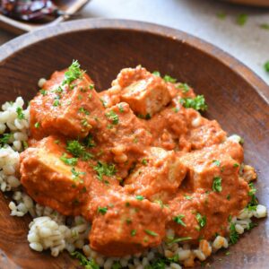 A wooden bowl filled with barley and a tofu in red arrabiata sauce, sprinkled with parsley