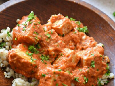 A wooden bowl filled with barley and a tofu in red arrabiata sauce, sprinkled with parsley