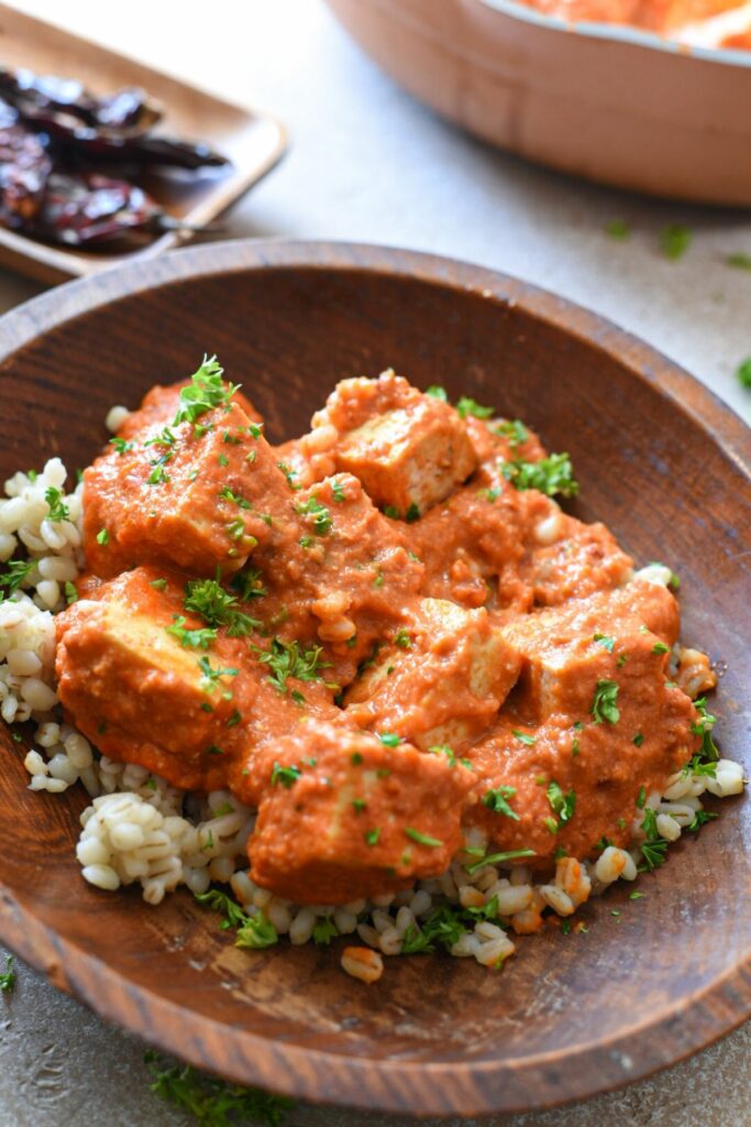 A wooden bowl filled with barley and a tofu in red arrabiata sauce, sprinkled with parsley