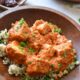 A wooden bowl filled with barley and a tofu in red arrabiata sauce, sprinkled with parsley