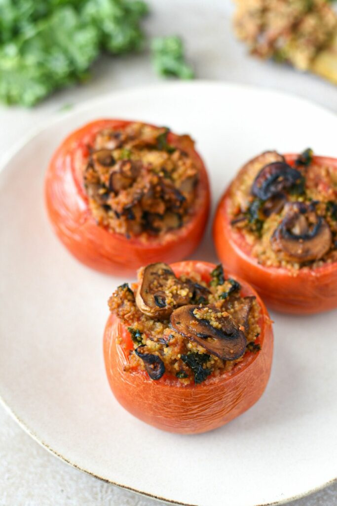 Three baked stuffed tomatoes on a white plate with kale in the background
