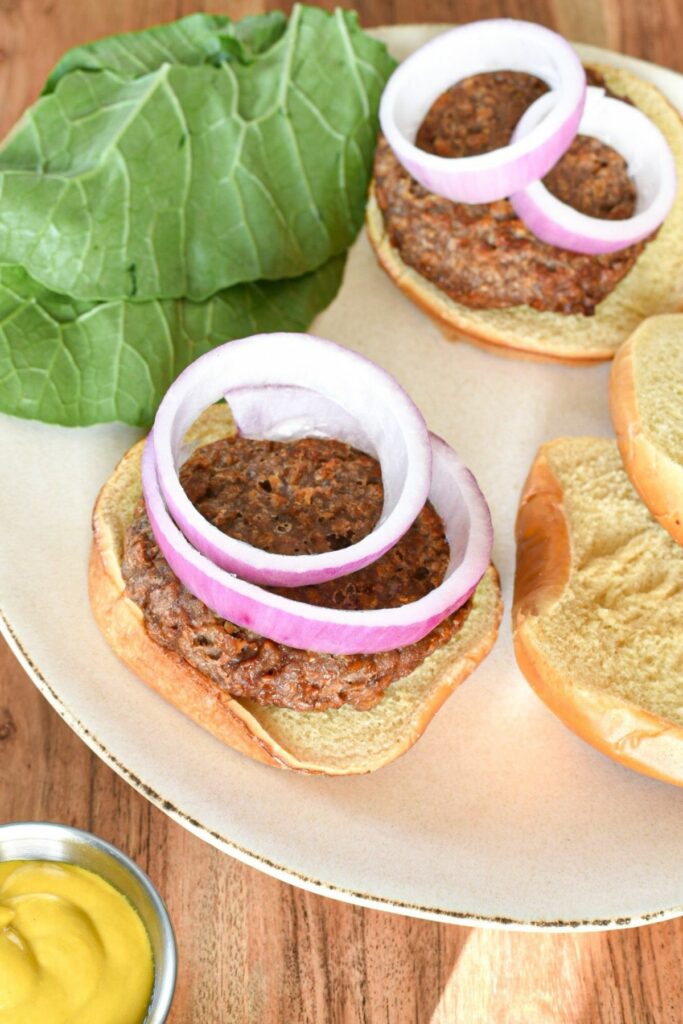 An overhead shot of a beyond meat burger on a burger bun with red onion slices and greens behind them, and mustard in the corner of the shot