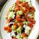 A plate filled with a greek layered dip with hummus, tzatziki, tomatoes, cucumber and olives
