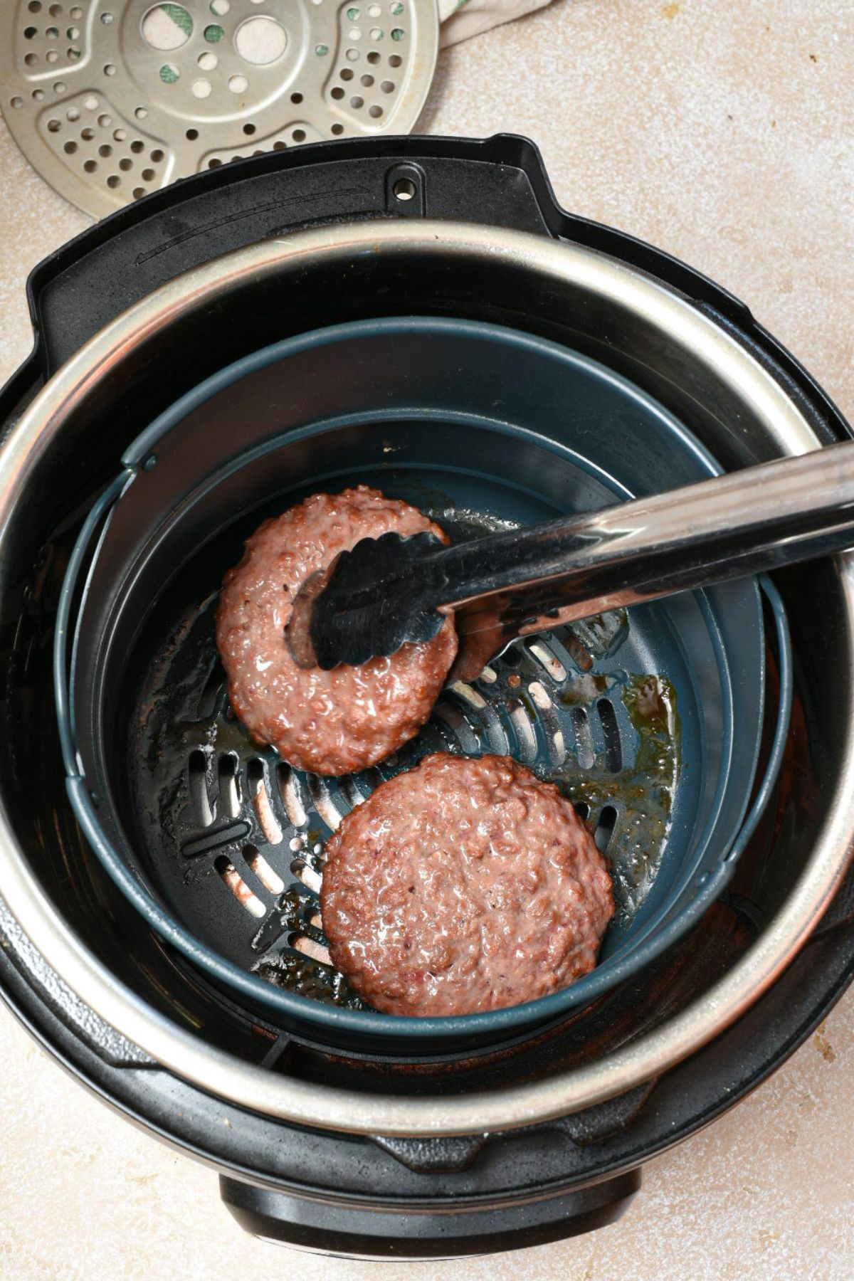 Tongs reaching into an air fryer basket to flip plant-based burgers