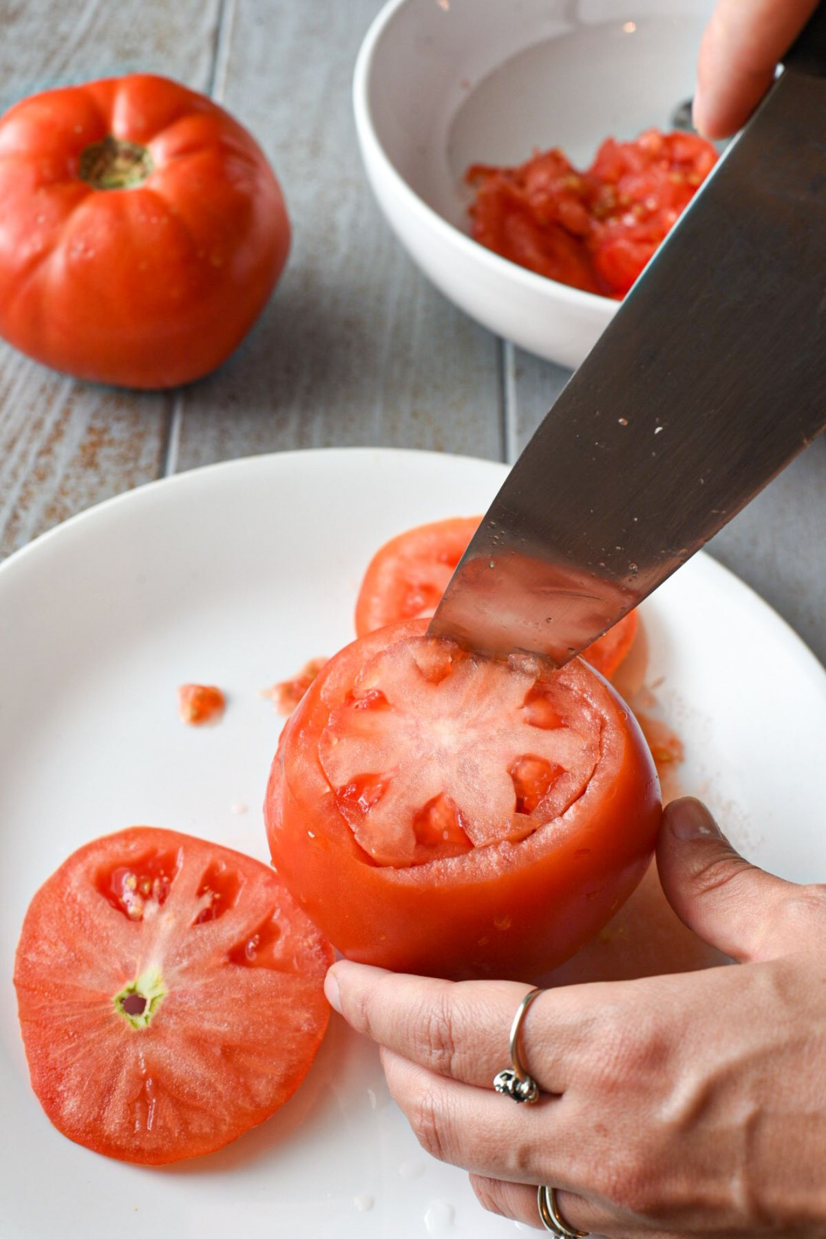 A knife cutting around the inside of a tomato to prepare to hollow out the inside