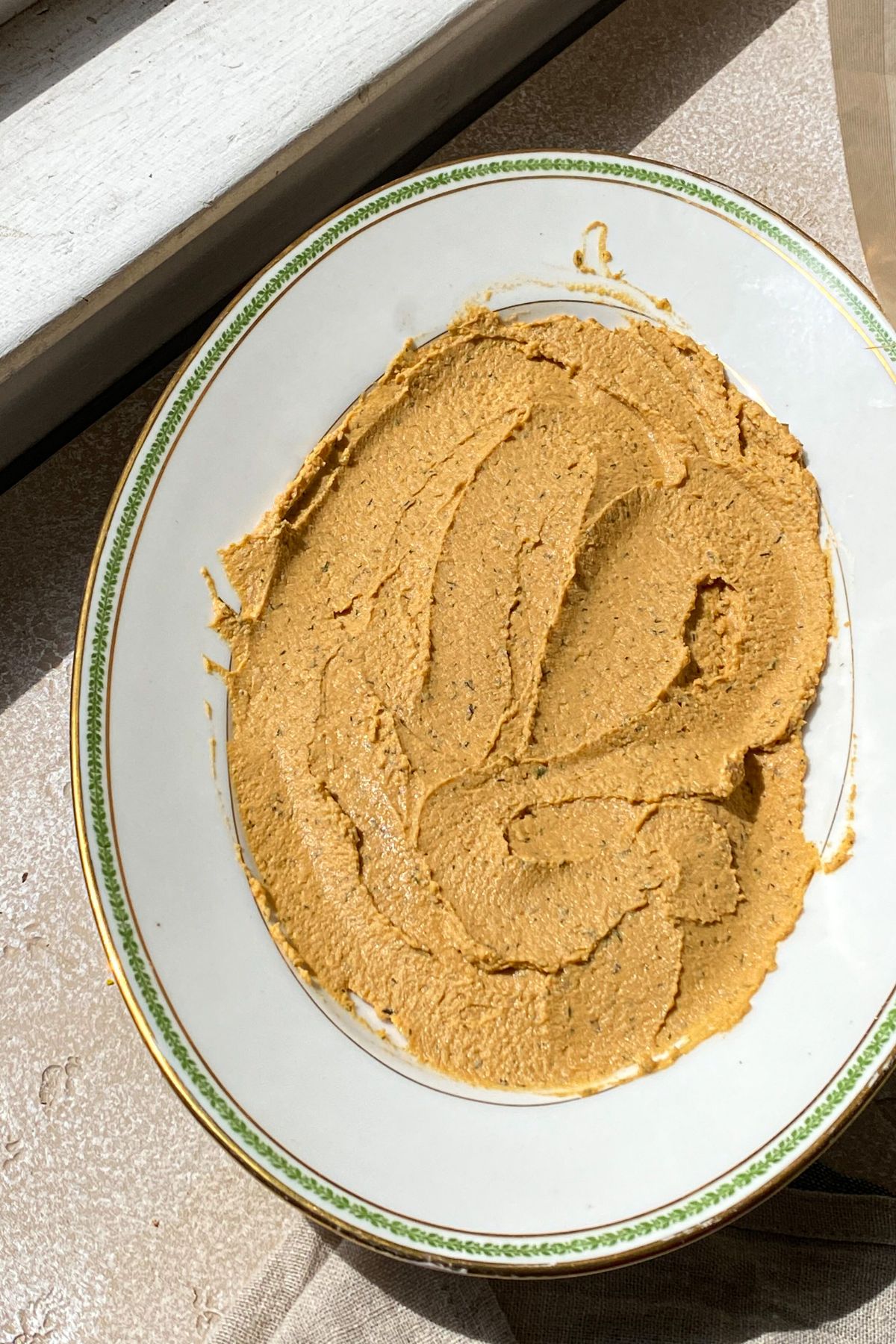 A white platter in the sun spread with roasted red pepper hummus in an oval shape