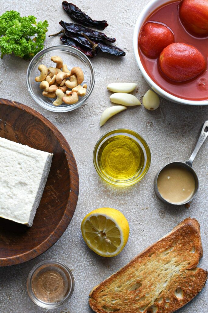 An overhead shot of ingredients used to make tofu and arrabiata sauce recipe, including tofu, plum tomatoes, toasted bread, dried serrano peppers