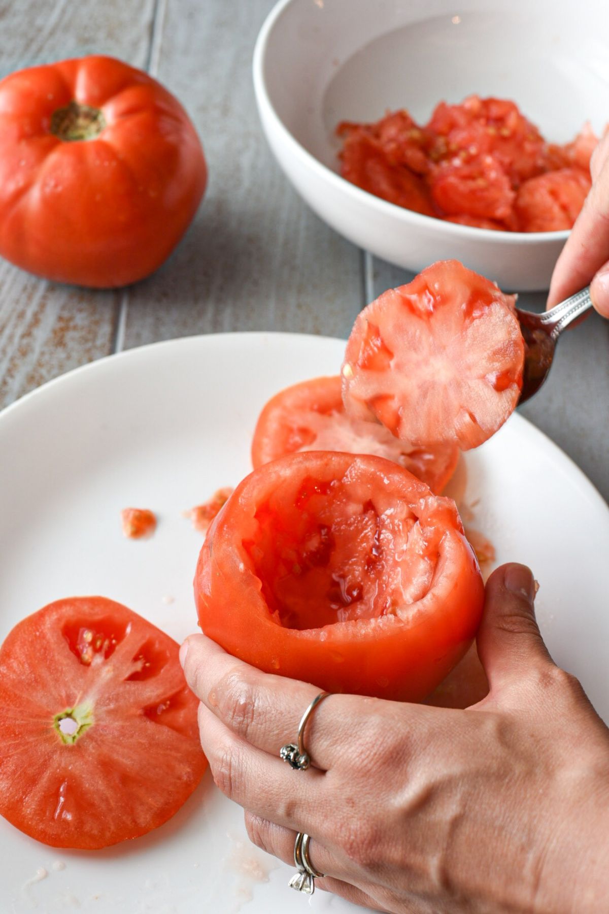A hand holding a large beefsteak tomato with the insides being scooped out by a spoon
