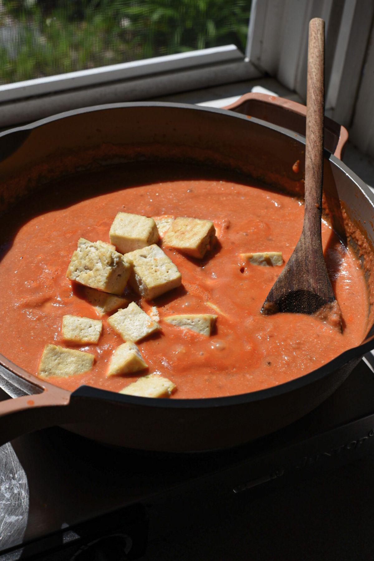 A pan in the sunlight filled with red sauce and cubed tofu.
