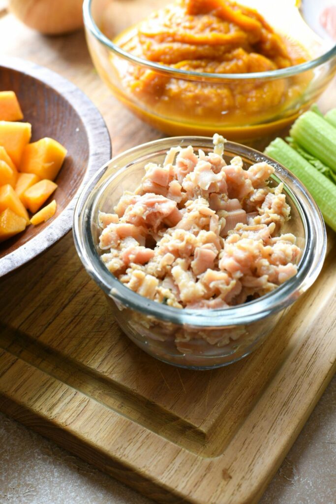 A glass bowl filled with chopped canned clams, with pumpkin puree in the background.