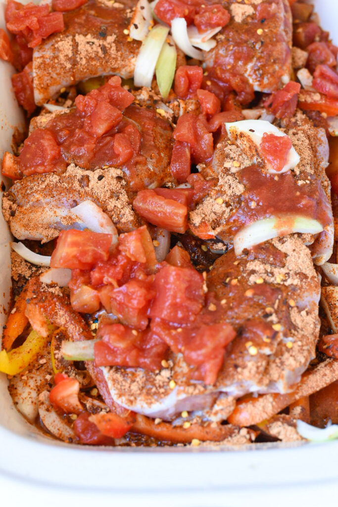 Chicken thighs in a slow cooker topped with spices and canned diced tomatoes