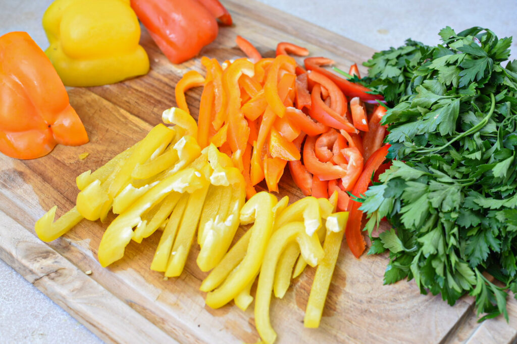 A wooden cutting board filled with sliced yellow, orange and red bell peppers and parsley