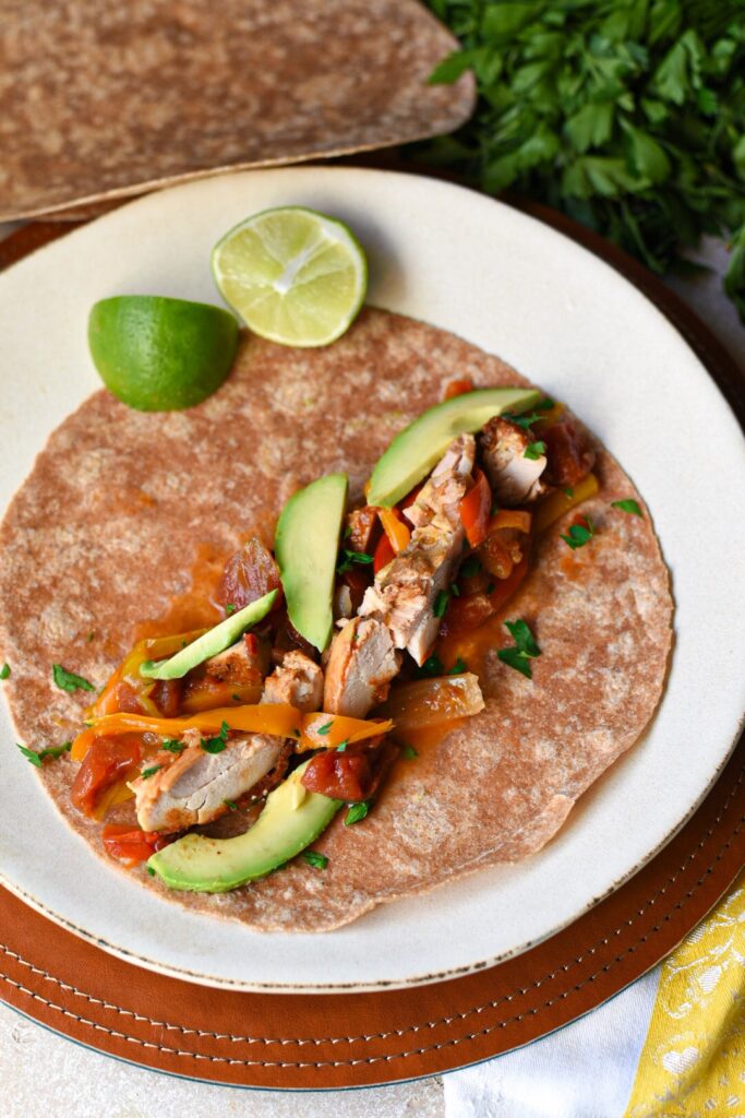 A whole wheat tortilla topped with crockpot chicken fajitas recipe with avocado and lime.