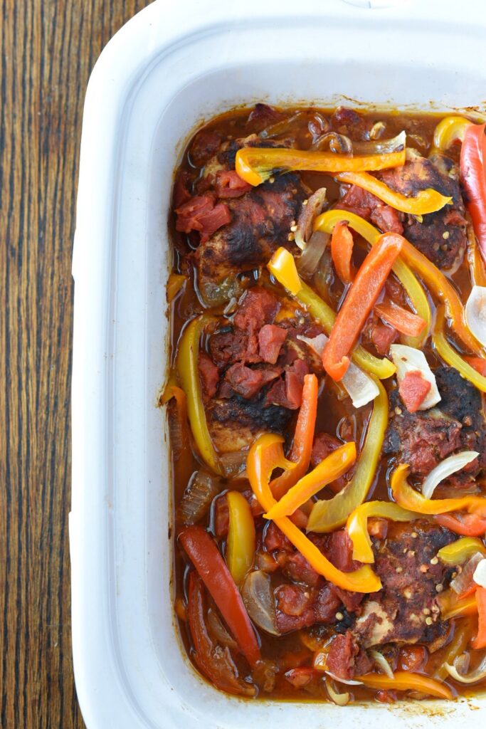 Half of a slow cooker filled with crockpot chicken fajitas topped with colorful bell peppers
