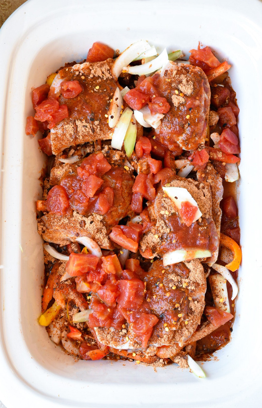 Chicken thighs in a crockpot topped with spices and diced tomatoes